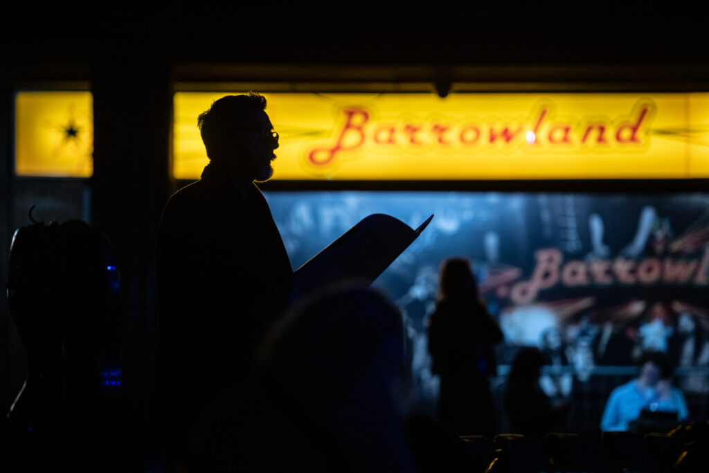 Silhouette of performer reading notes, in front of illuminated Barrowlands sign