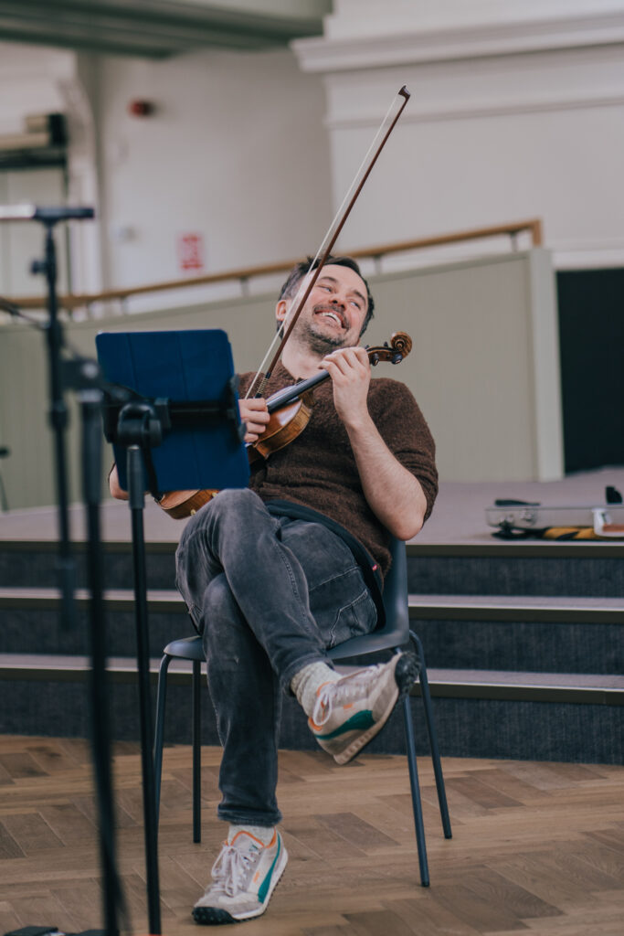Violinist Donald Grant, leaning back and laughing during a break in concert rehearsals.