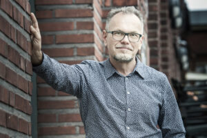 Photo of Jarmo Eskelinen leaning with one hand against brick wall